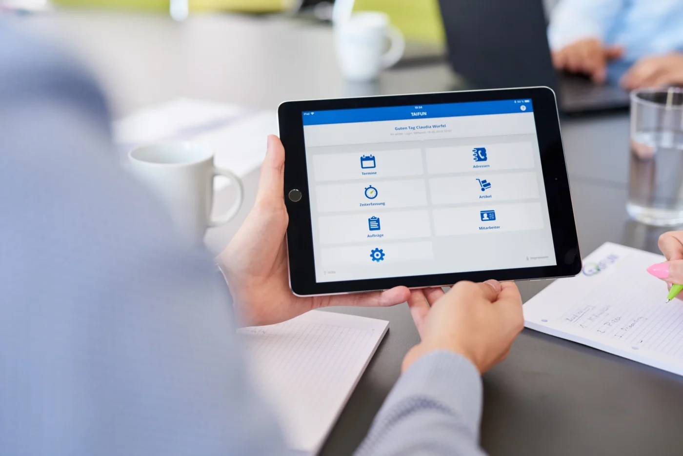 Zwei Hände halten ein mobiles Tablet, welches Software abbildet.