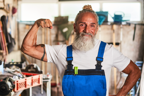 Ein Handwerker zeigt stolz seine Kraft beim Arbeiten in der Werkstatt - im Hintergrund Werkzeug und Maschinen.