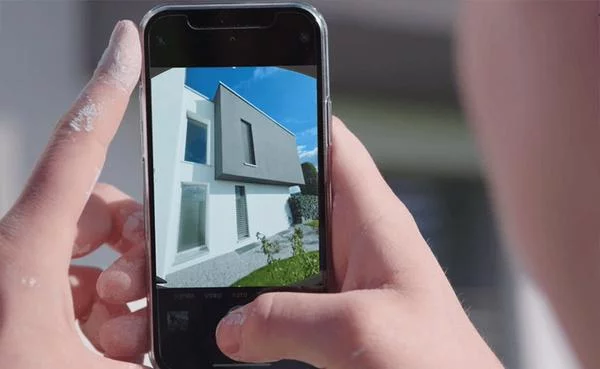 Jemand fotografiert mit dem Handy ein Gebäude mit klaren Linien und modernen Formen - draußen auf der Baustelle.