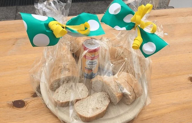 Jemand richtet auf einem Holztisch Brot und Salz auf einem Holztablett an und verpackt alles sorgfältig mit Schleifen.