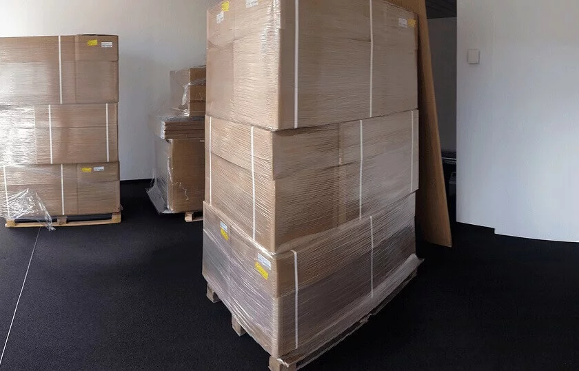 Jemand stapelt große Kartons auf Paletten und bereitet sie im Lager für den nächsten Einsatz vor.