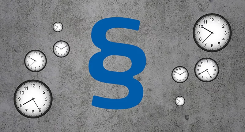 Mehrere Uhren zeigen verschiedene Zeiten, im Mittelpunkt steht ein großes, blaues Paragraphenzeichen auf grauem Grund.